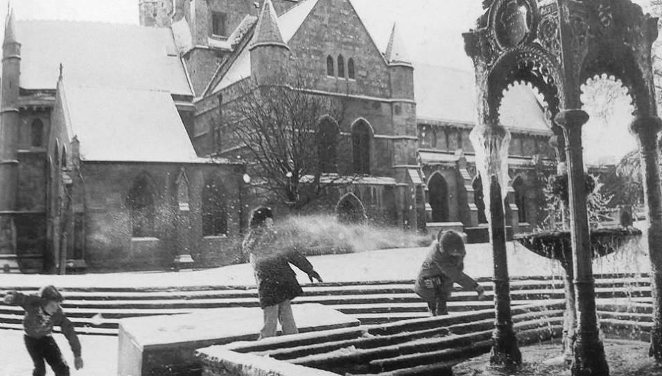 Children playing in snow in front of a church, near a frozen fountain.
