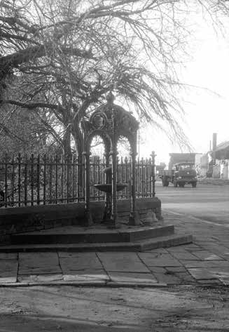 Black and white photo of a decorative fountain in a small town, with a road and bare trees.