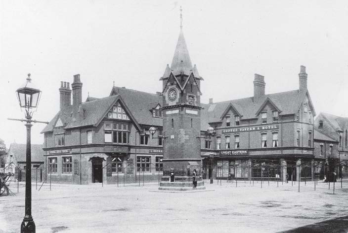 Clock tower and buildings in a town square, likely early 20th century. Includes streetlights.