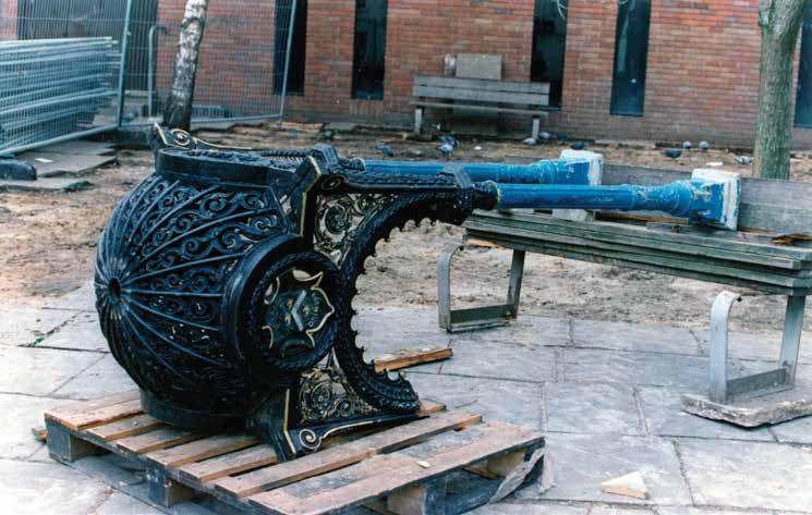 Ornate black cast iron fountain base on a wooden pallet, with blue pipes resting on a wooden table.
