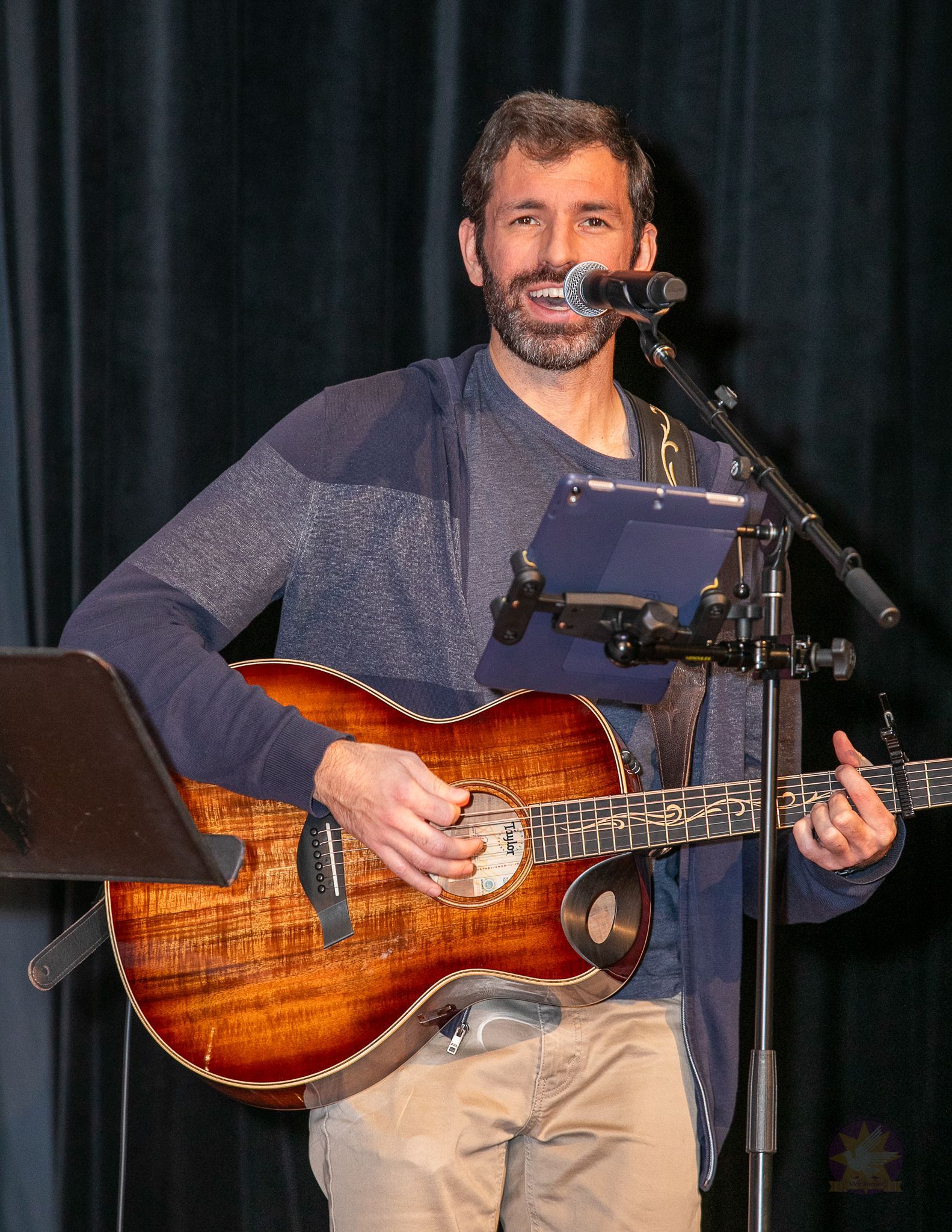 Man playing an acoustic guitar and singing into a microphone onstage