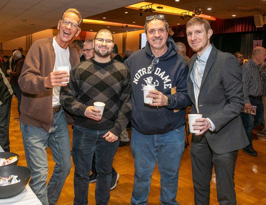 Four people standing indoors, smiling and holding drinks at a casual event.