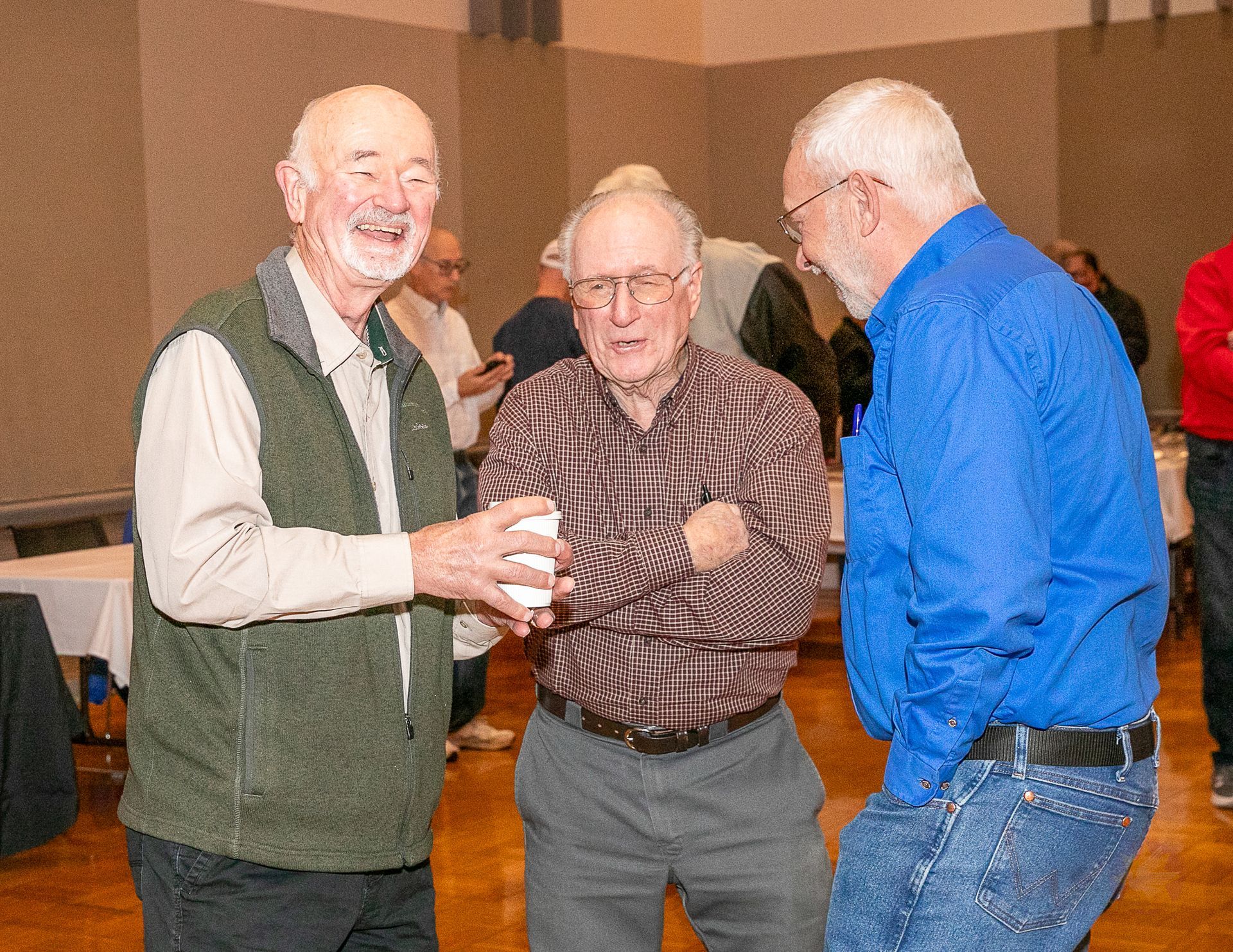 Three people chatting at an indoor gathering, two smiling and one in a bright blue shirt.
