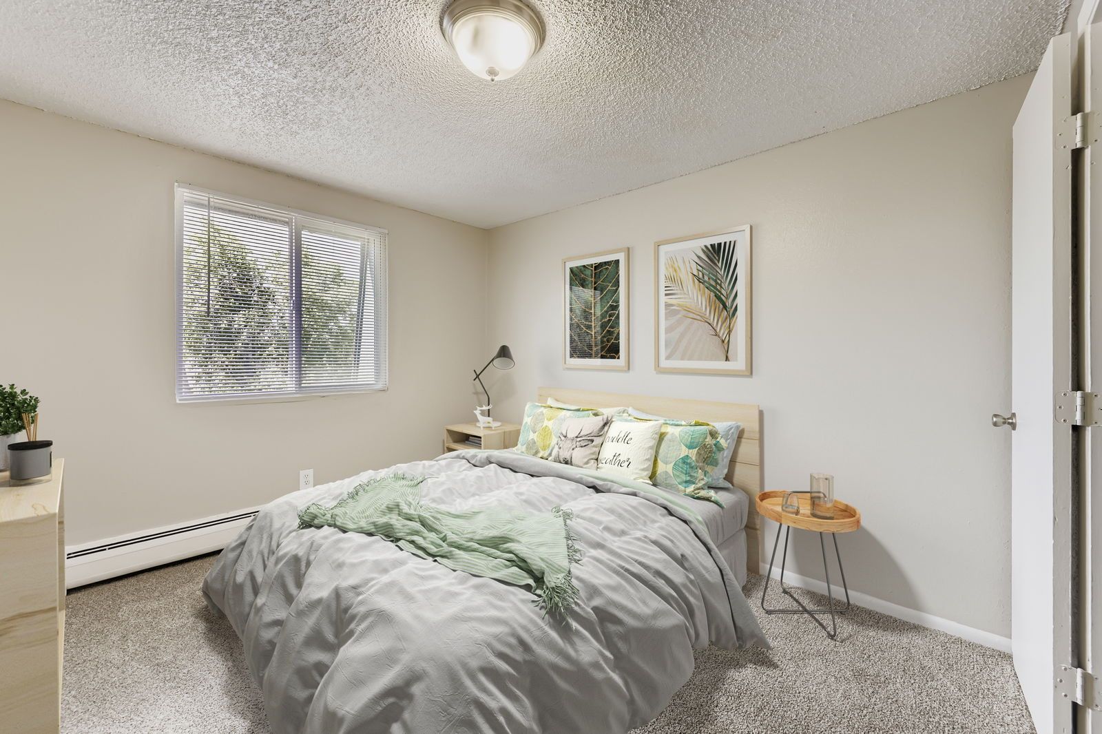 Bedroom in an apartment with a neatly made bed, two framed prints, and a window with blinds.