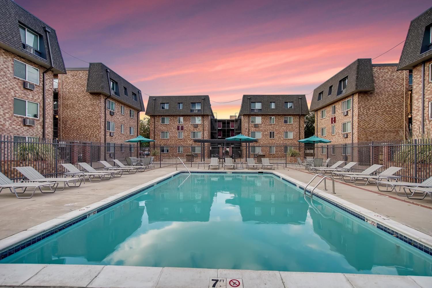 Outdoor community swimming pool surrounded by lounge chairs and brick apartment buildings.