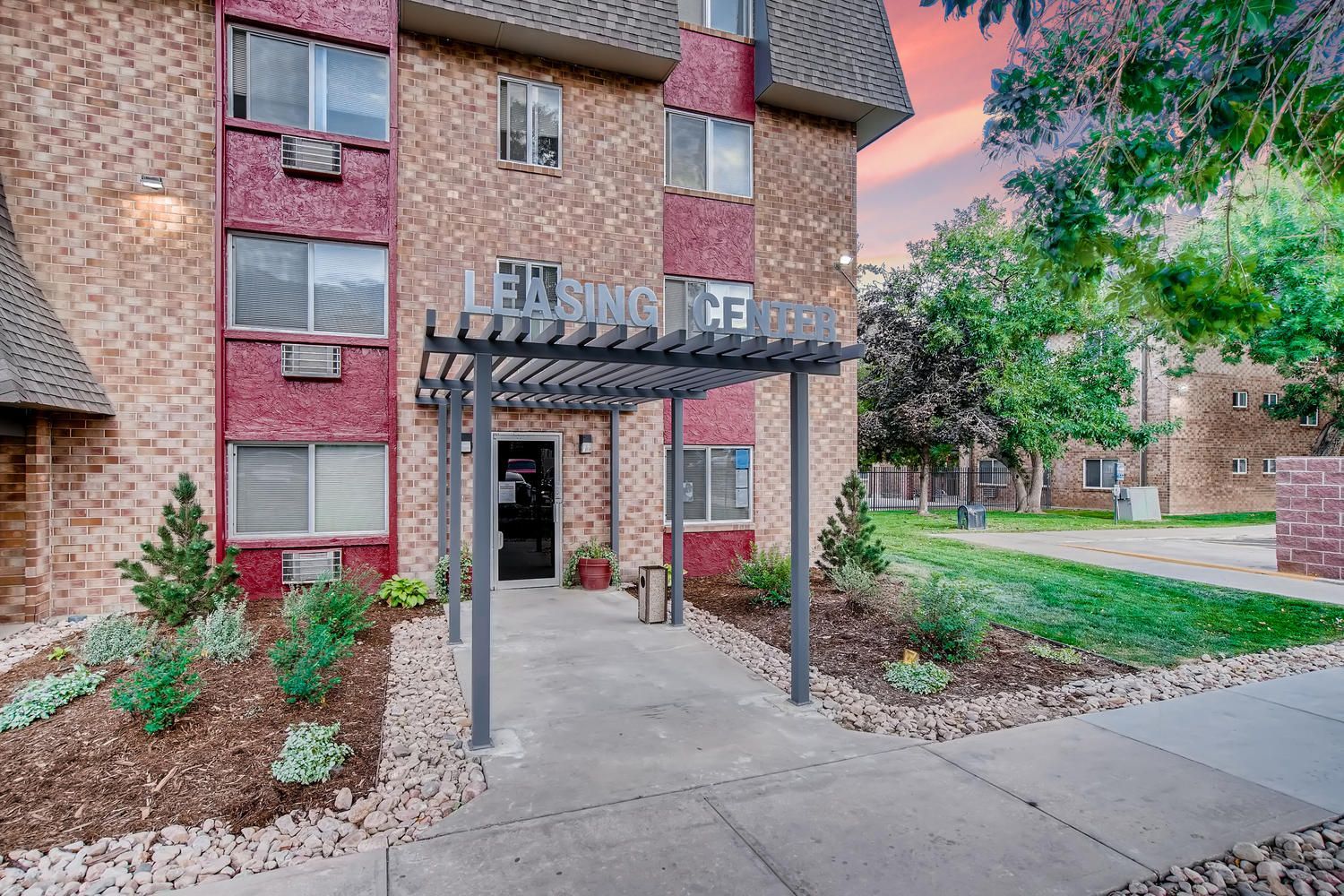 Exterior of an apartment building with a leasing center entrance canopy and landscaped walkway.