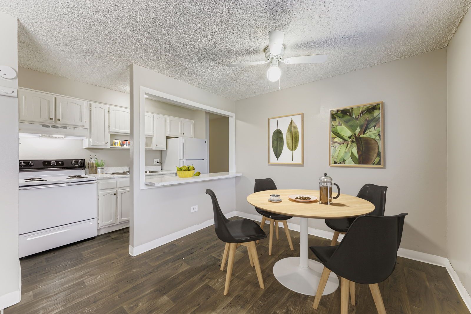 Dining area and kitchen in an apartment, round table with four chairs and white cabinets.