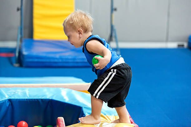 A young boy is standing on a balance beam holding a ball.