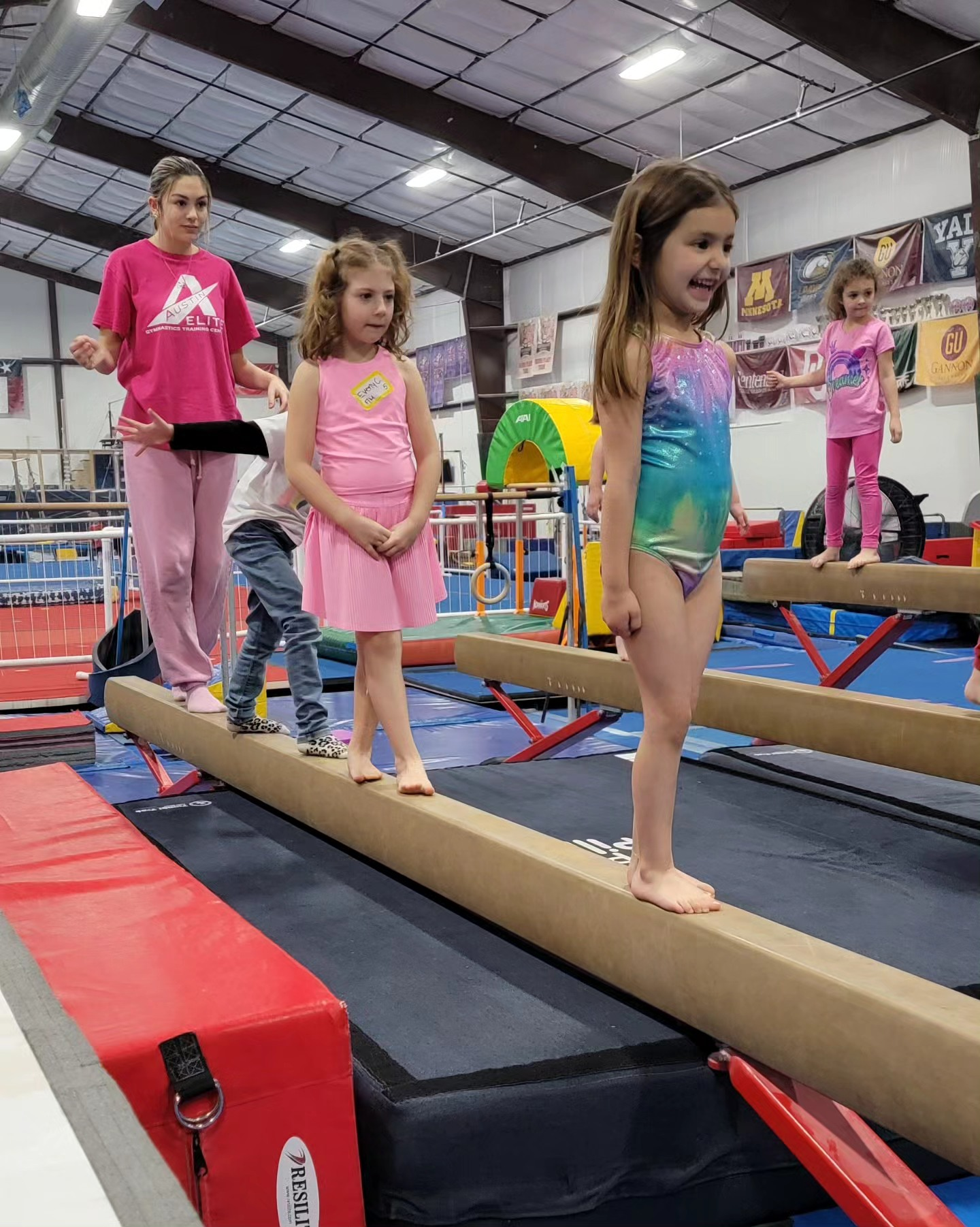 A group of young girls are standing on a balance beam in a gym.