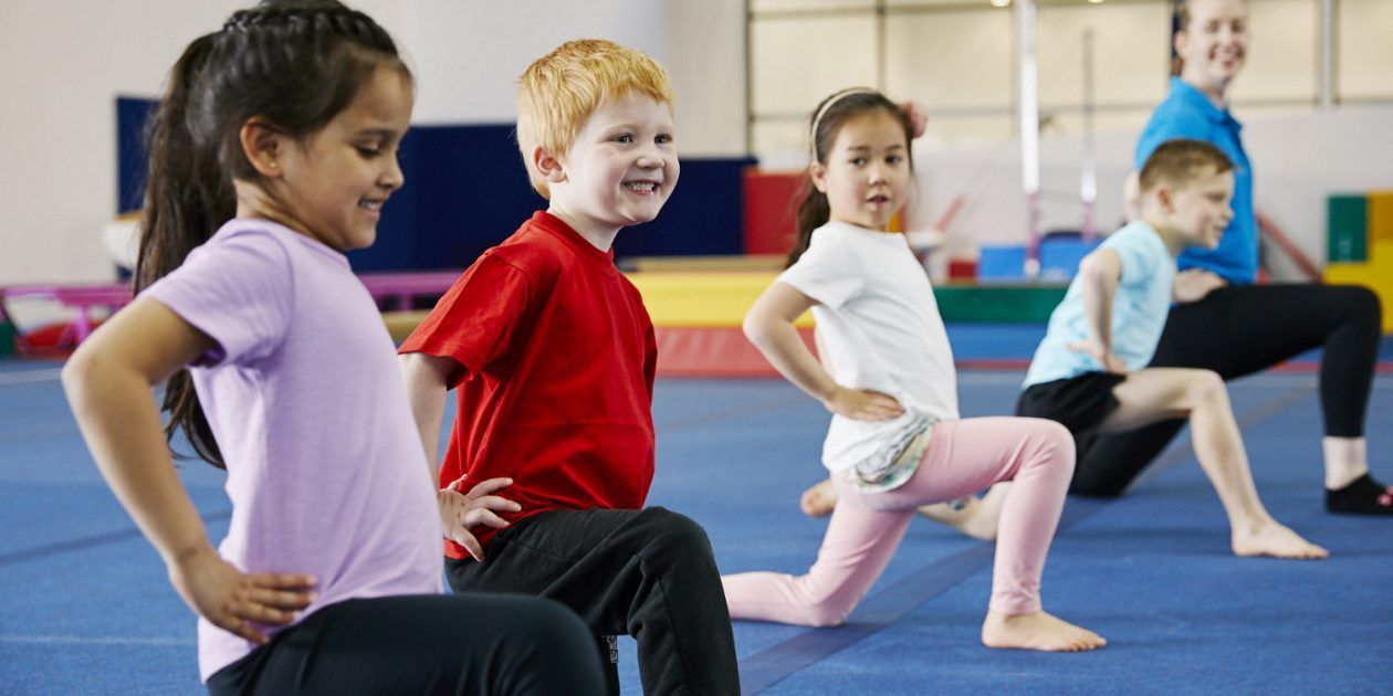 A group of children are doing stretching exercises in a gym.