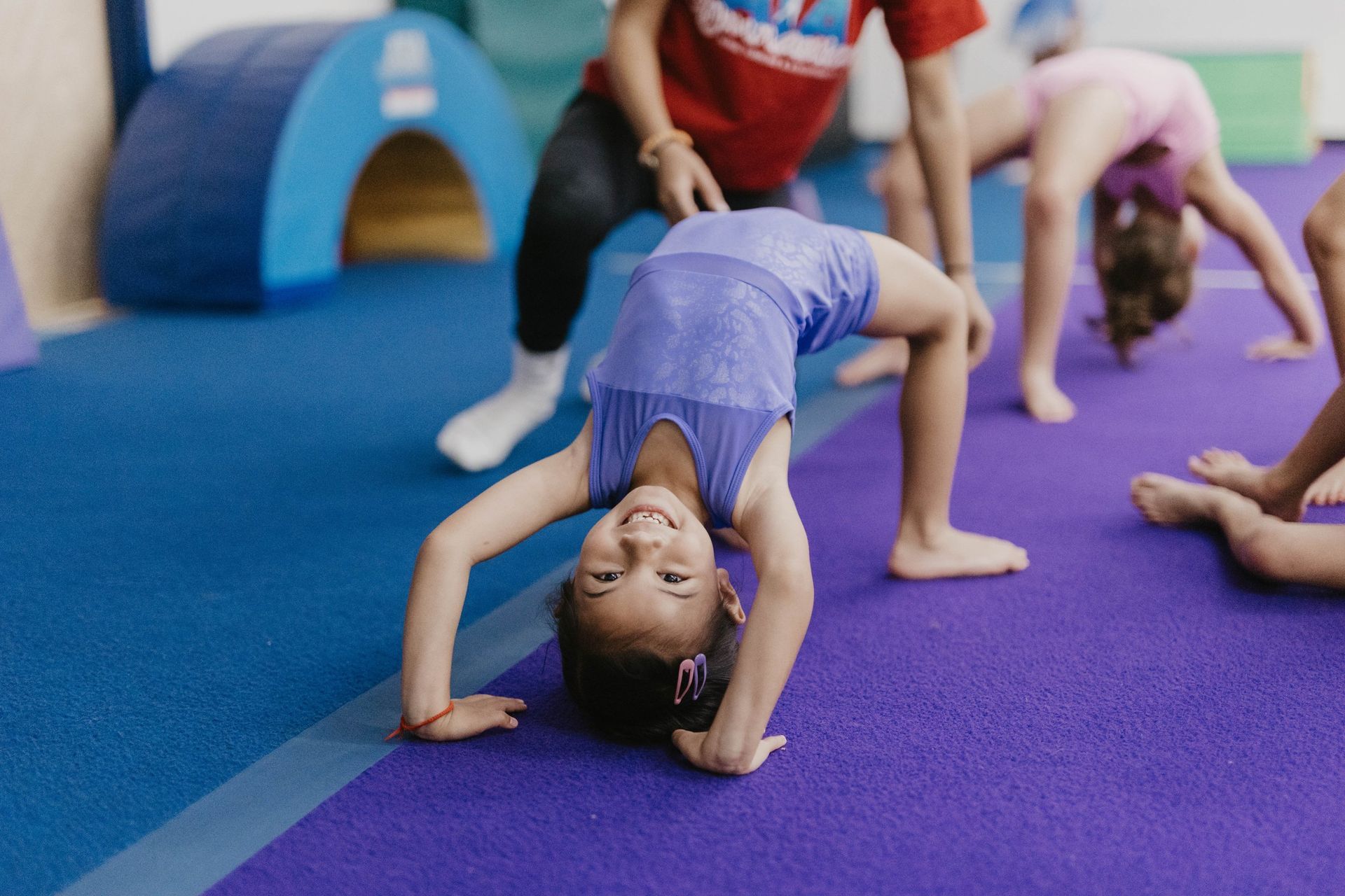 A little girl is doing a handstand on a purple mat in a gym.