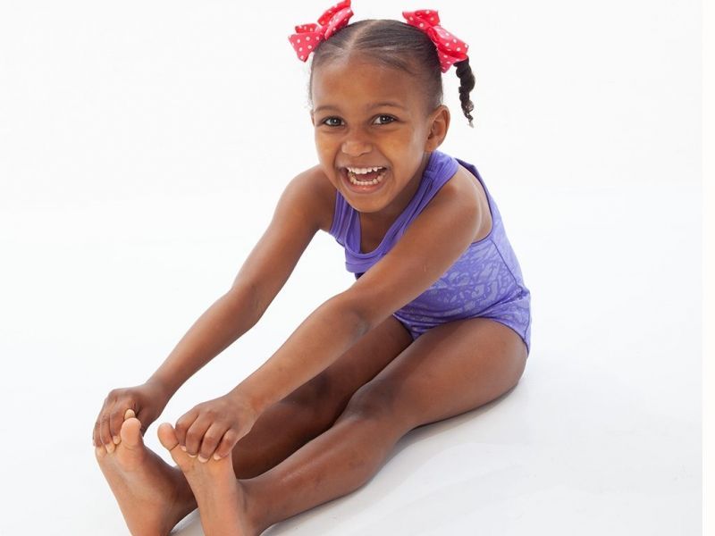 A little girl is sitting on the floor stretching her legs