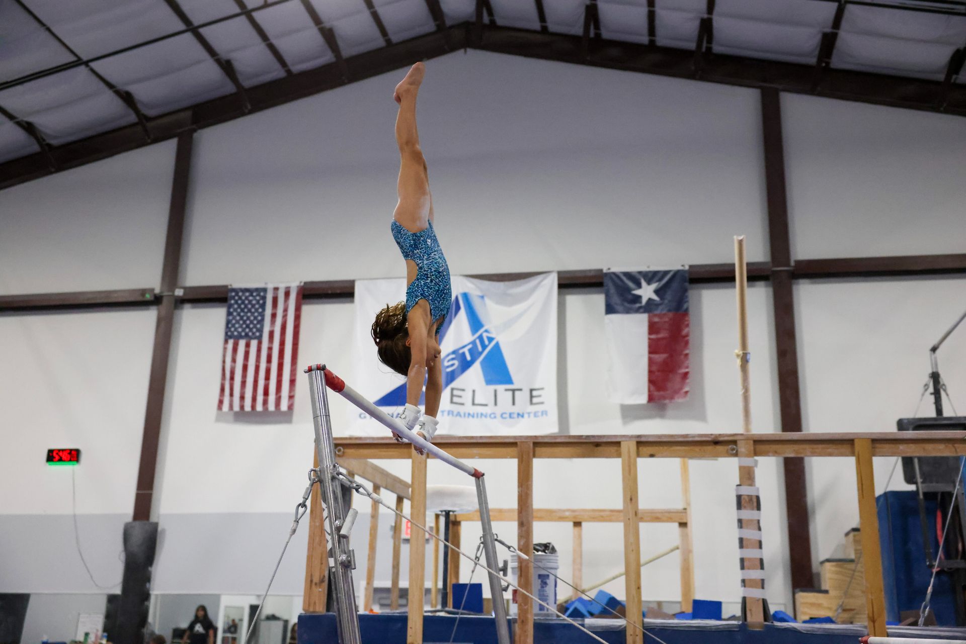 A gymnast is doing a handstand on a parallel bars in a gym.