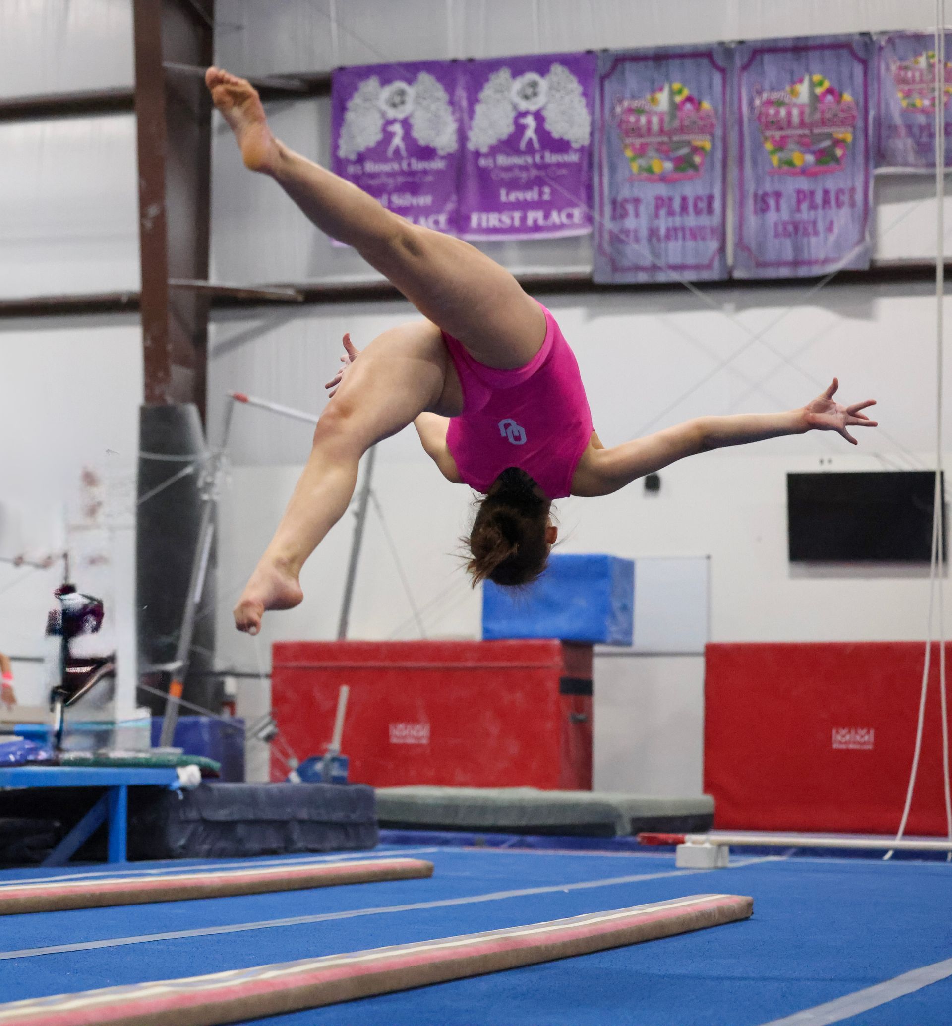 A woman in a pink leotard is doing a trick on a balance beam