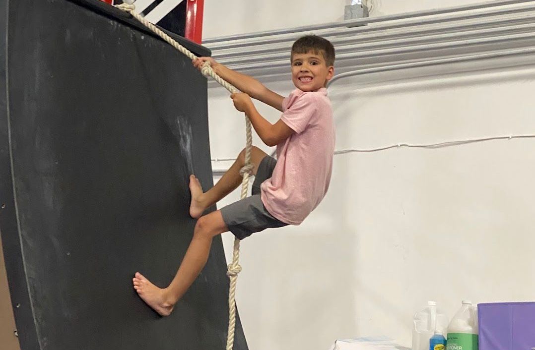 A young boy is climbing a rope wall in a gym.