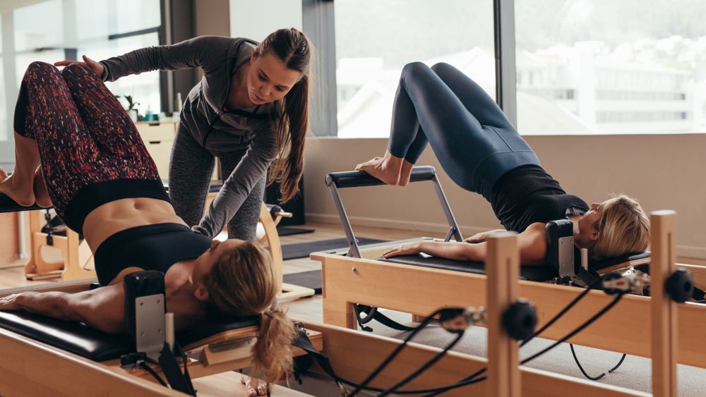 A woman is teaching two women how to do pilates on a pilates machine — 360 Fitness Group in Cairns, QLD