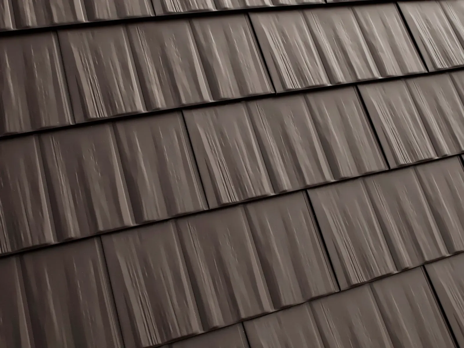 Close-up view of overlapping dark brown metal roofing tiles with a textured, vertically ribbed cedar shingle pattern.