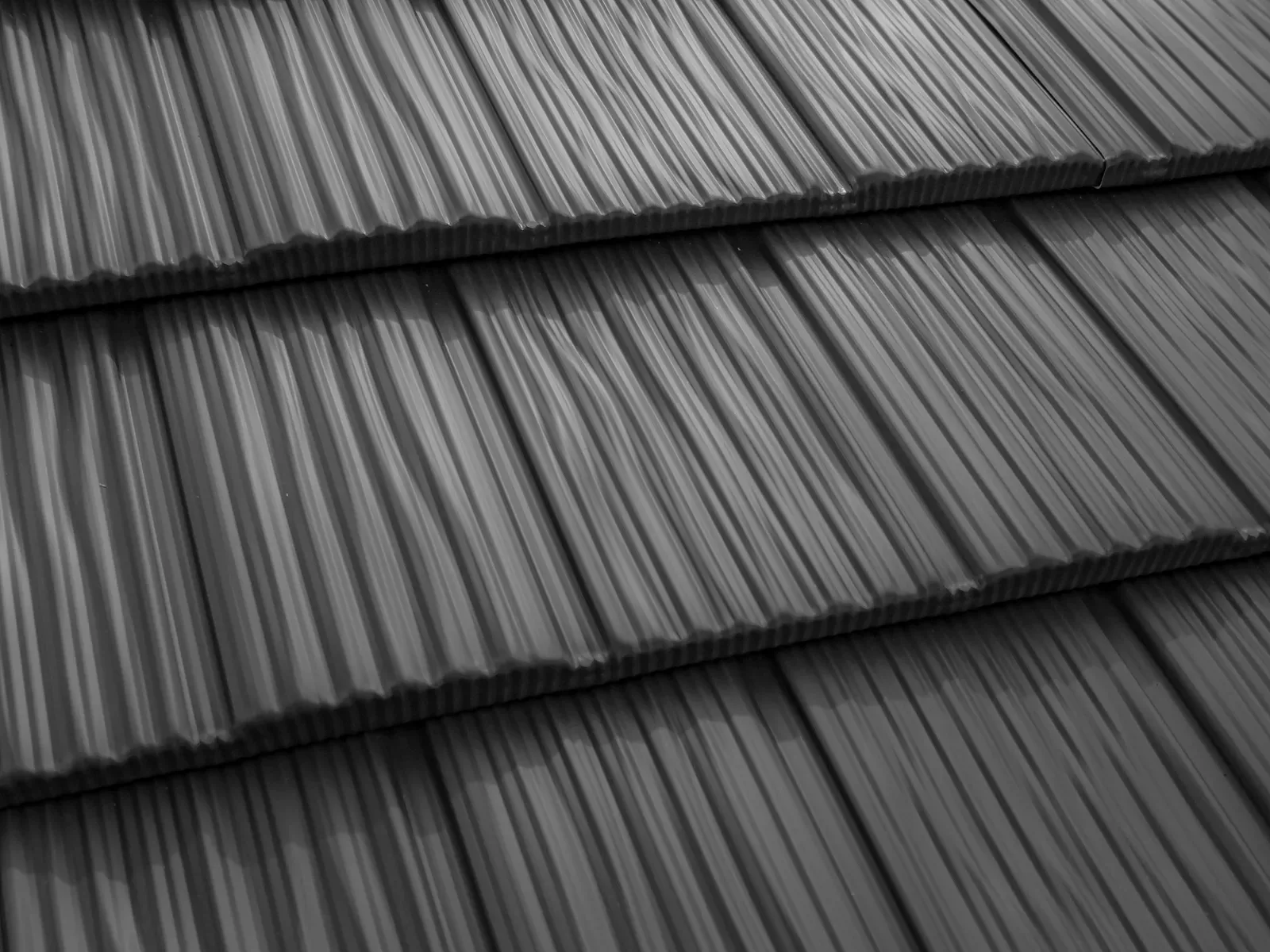 Close-up of overlapping black, wood-textured roof shingles arranged in horizontal rows.