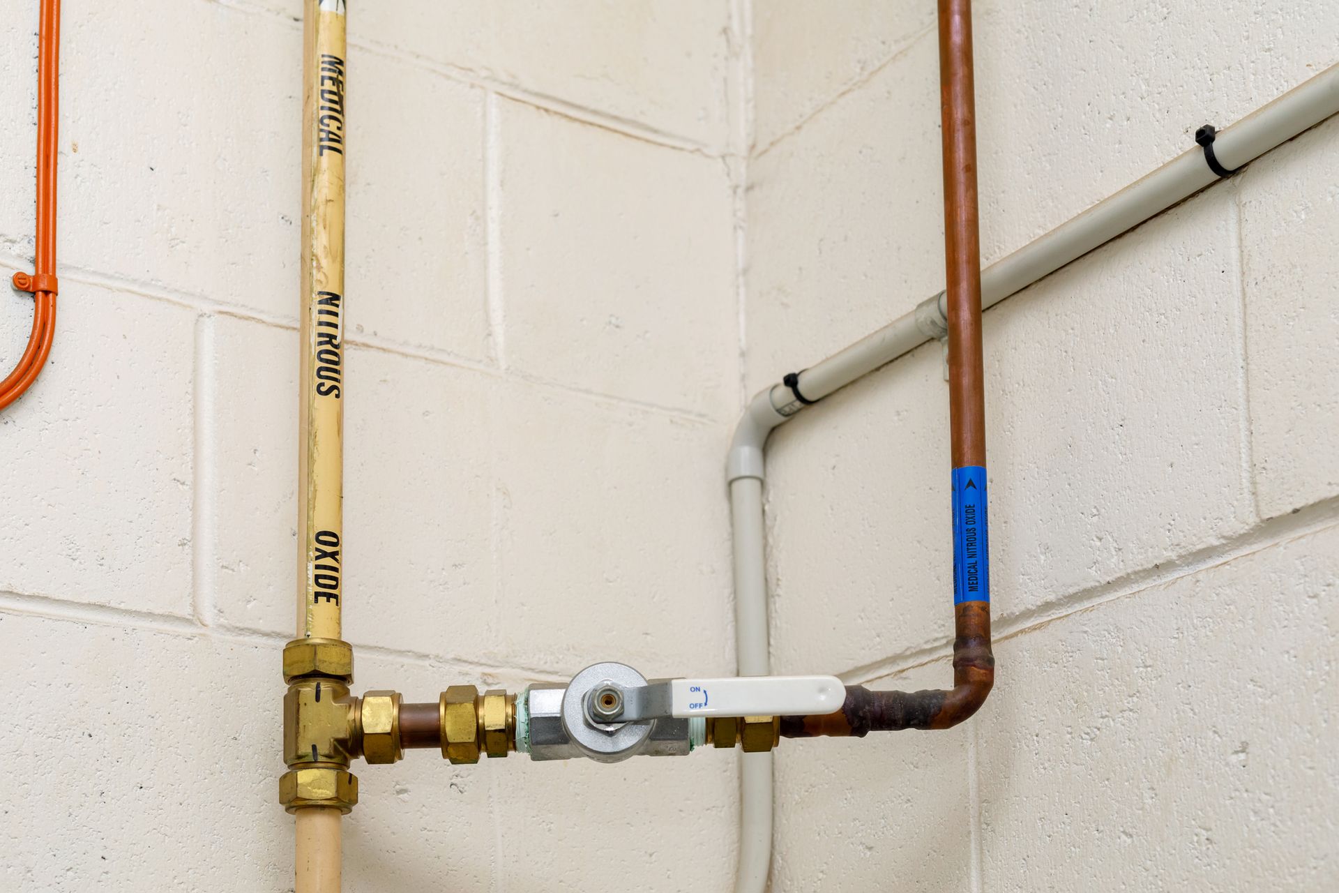 A smiling male plumber in a hard hat and vest, working on plumbing, with a gauge and pipes visible.