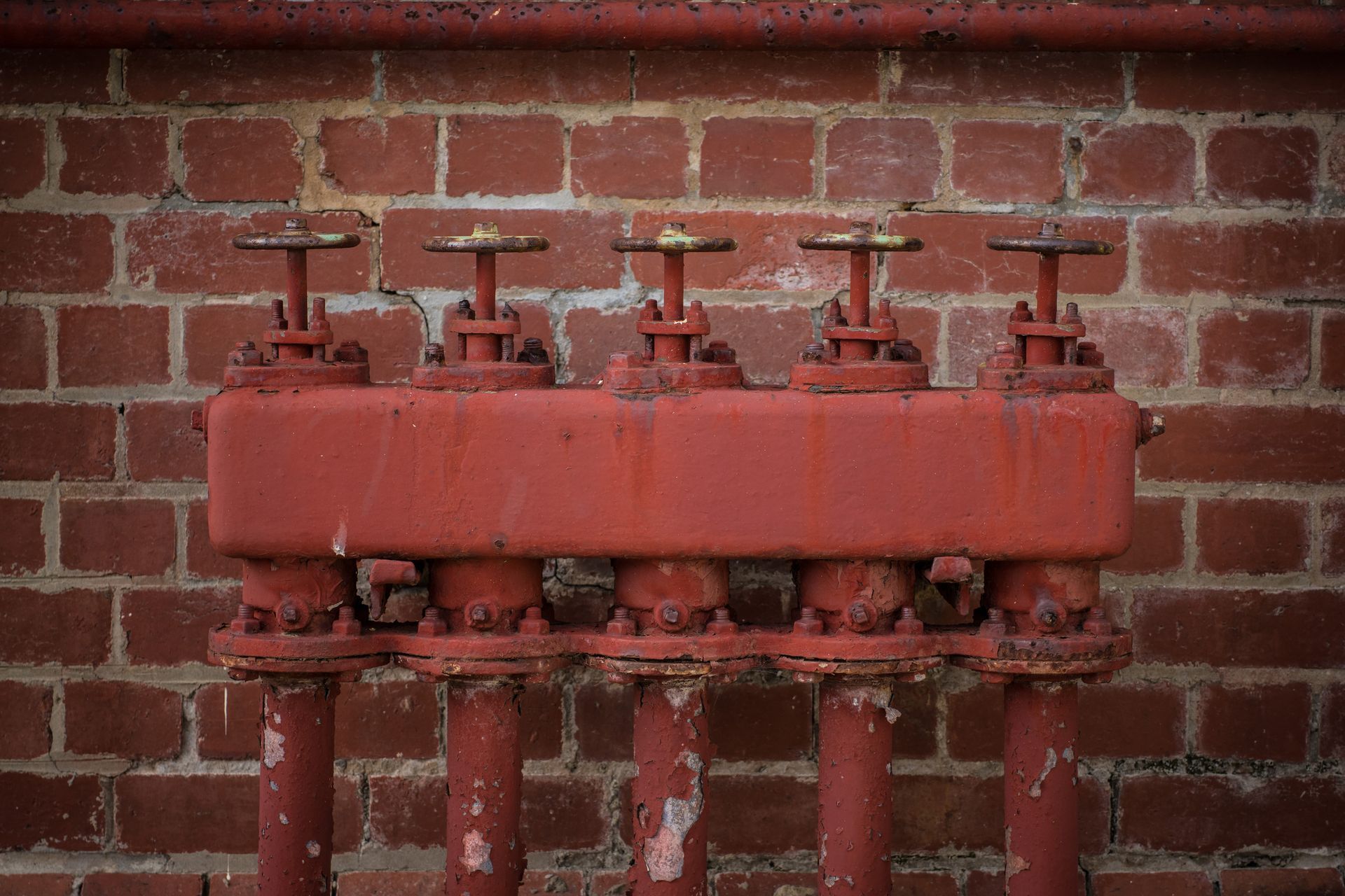 A row of red pipes against a brick wall.
