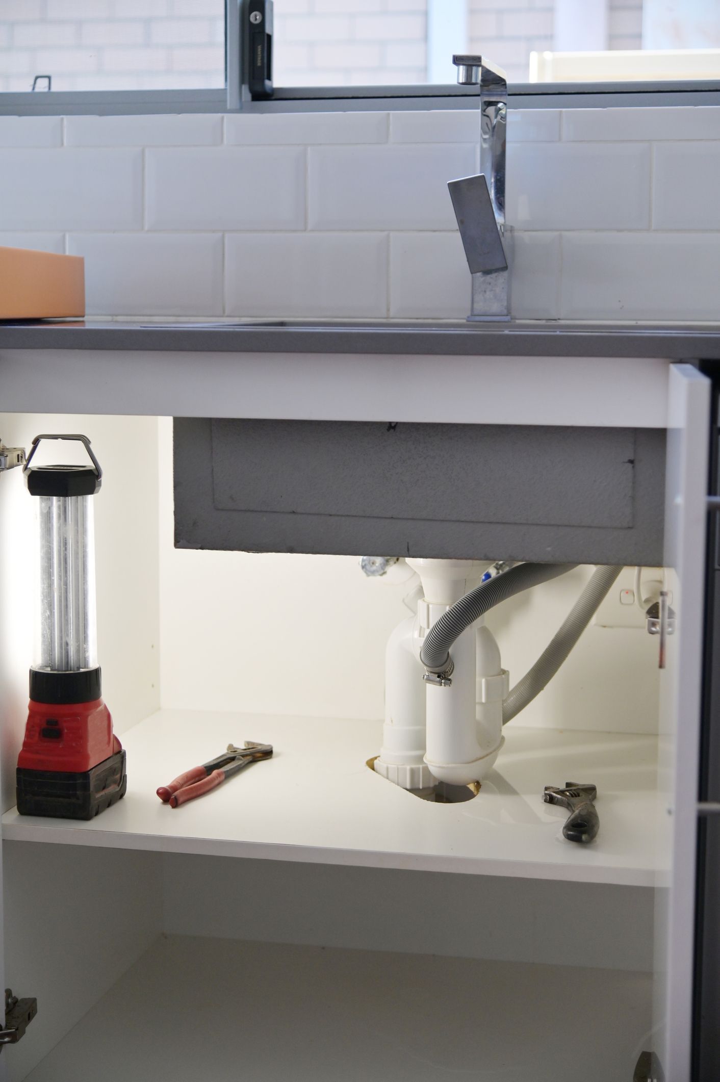Plumber working under a sink with a wrench. A toolbox sits open nearby.