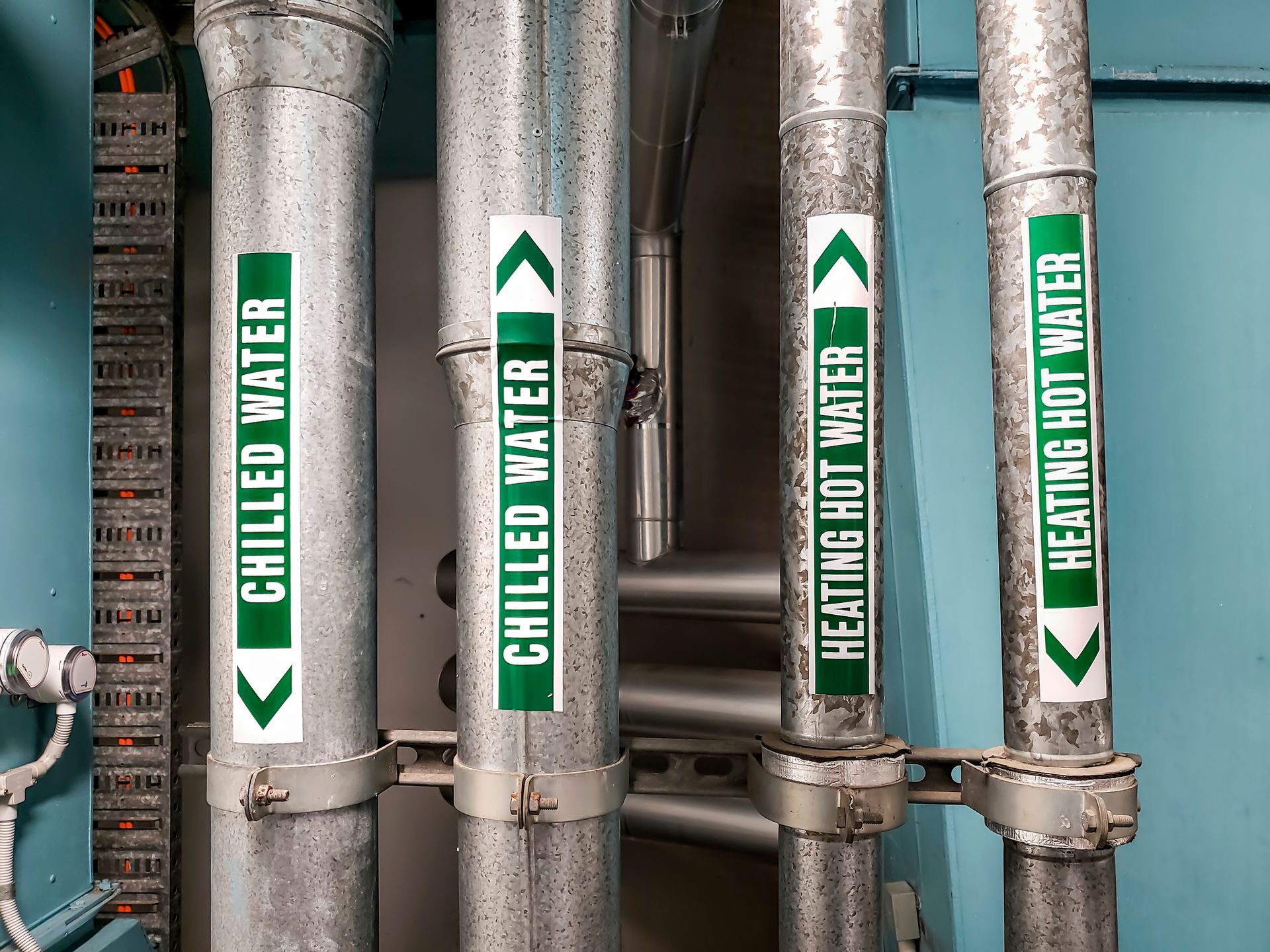 A plumber in a blue jumpsuit is fixing a bathroom faucet in a bright bathroom with a window and a towel rack.