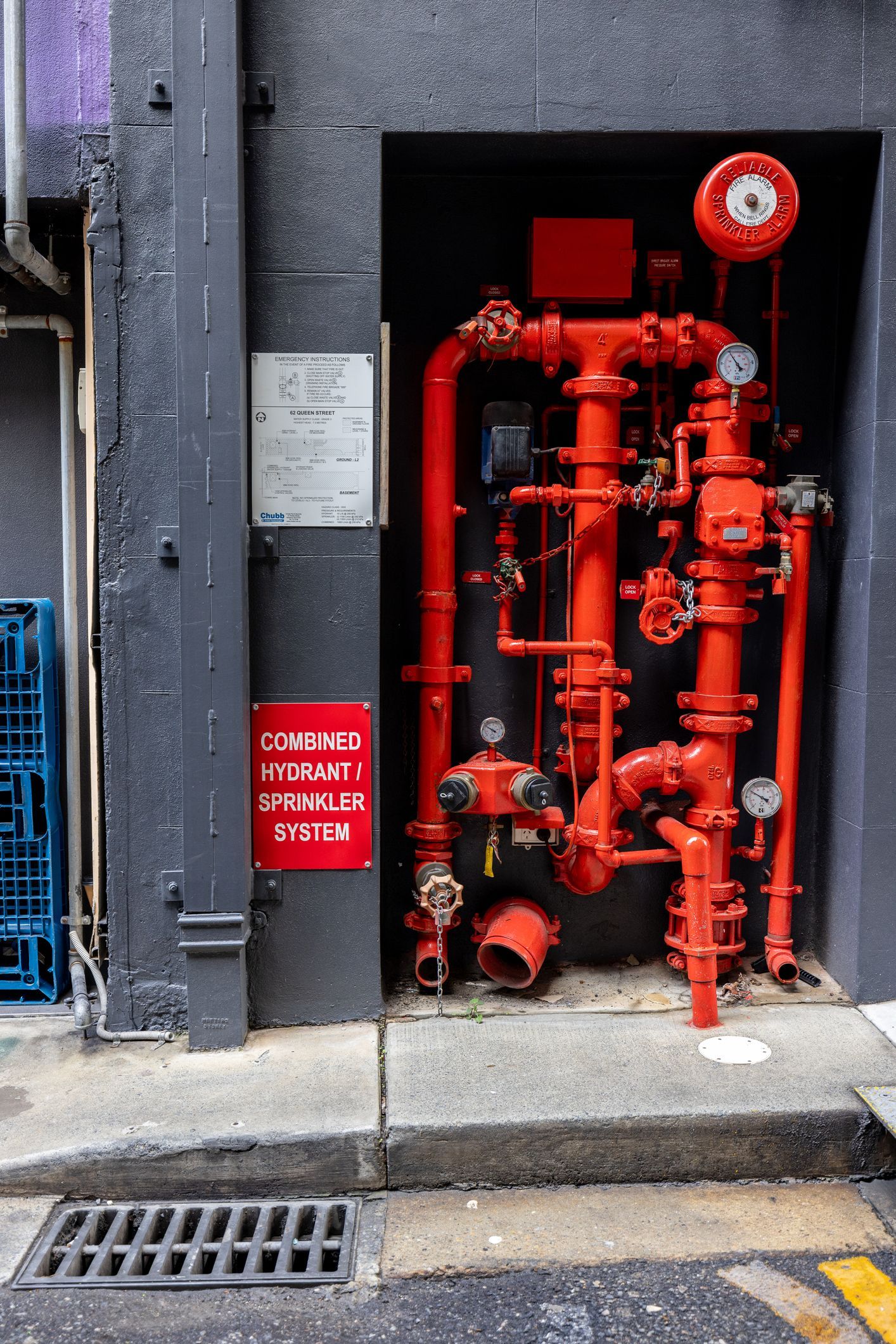 A plumber kneeling under a bathroom sink, using a wrench to repair a pipe. He wears a gray shirt and jeans.