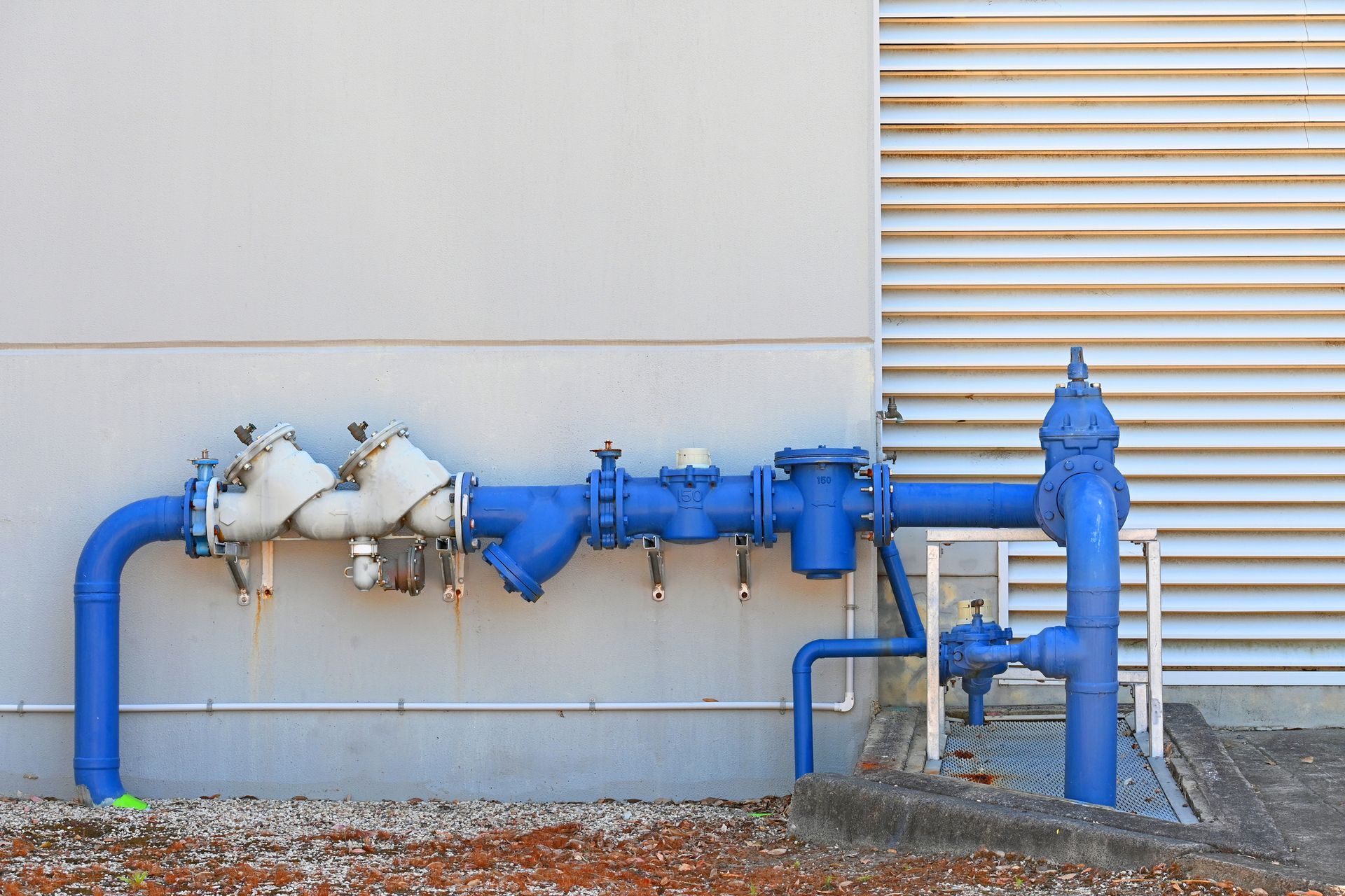 A man in a blue uniform uses pliers to work on copper pipes connected to a white appliance.