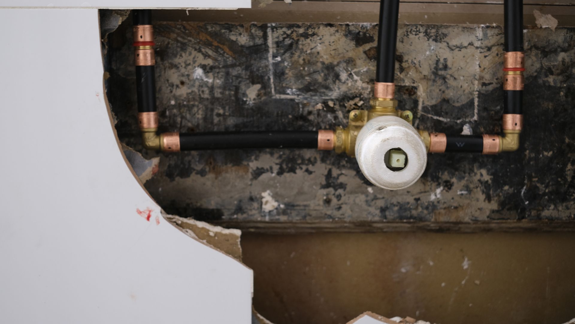 A plumber kneels by a sink, inspecting the pipes and taking notes in a bathroom with red tile flooring.