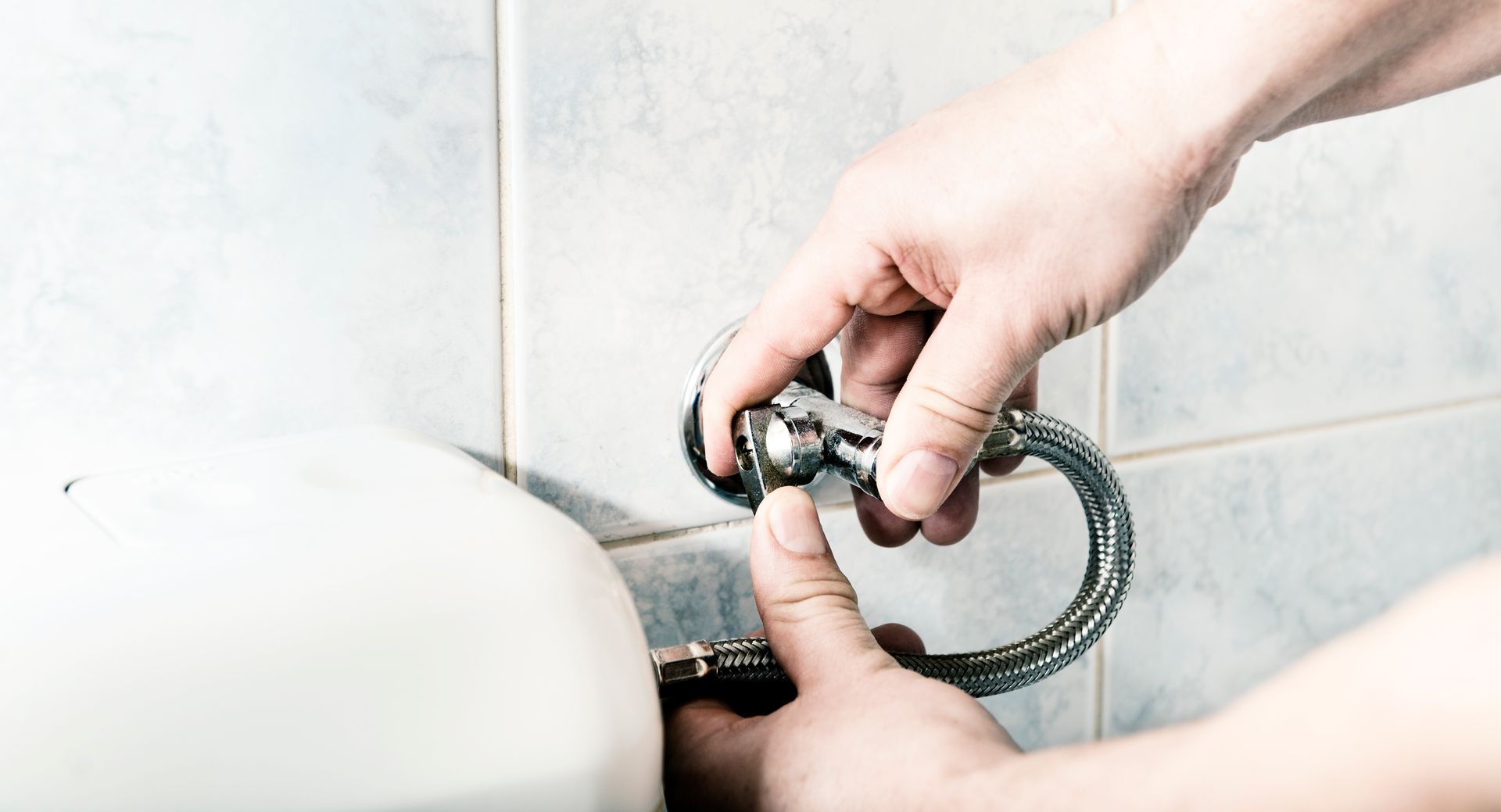 Hands installing a chrome towel ring on a tiled wall next to a white sink.