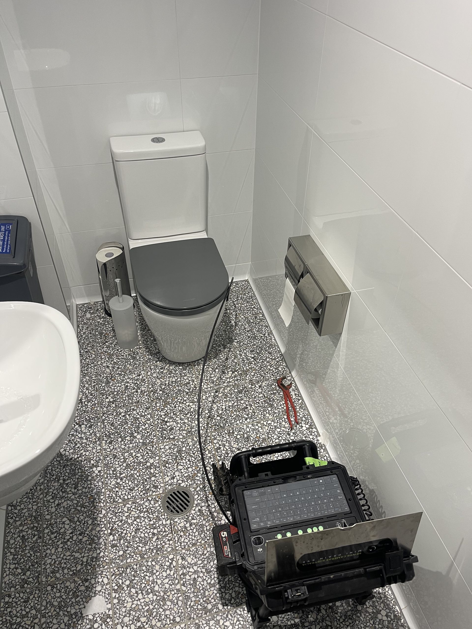 A bathroom with a toilet , sink and a camera on the floor.
