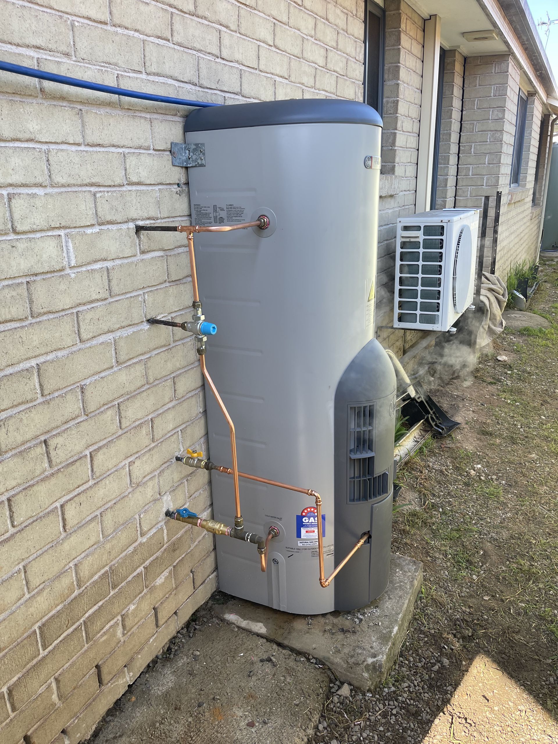 A water heater is attached to the side of a brick building.