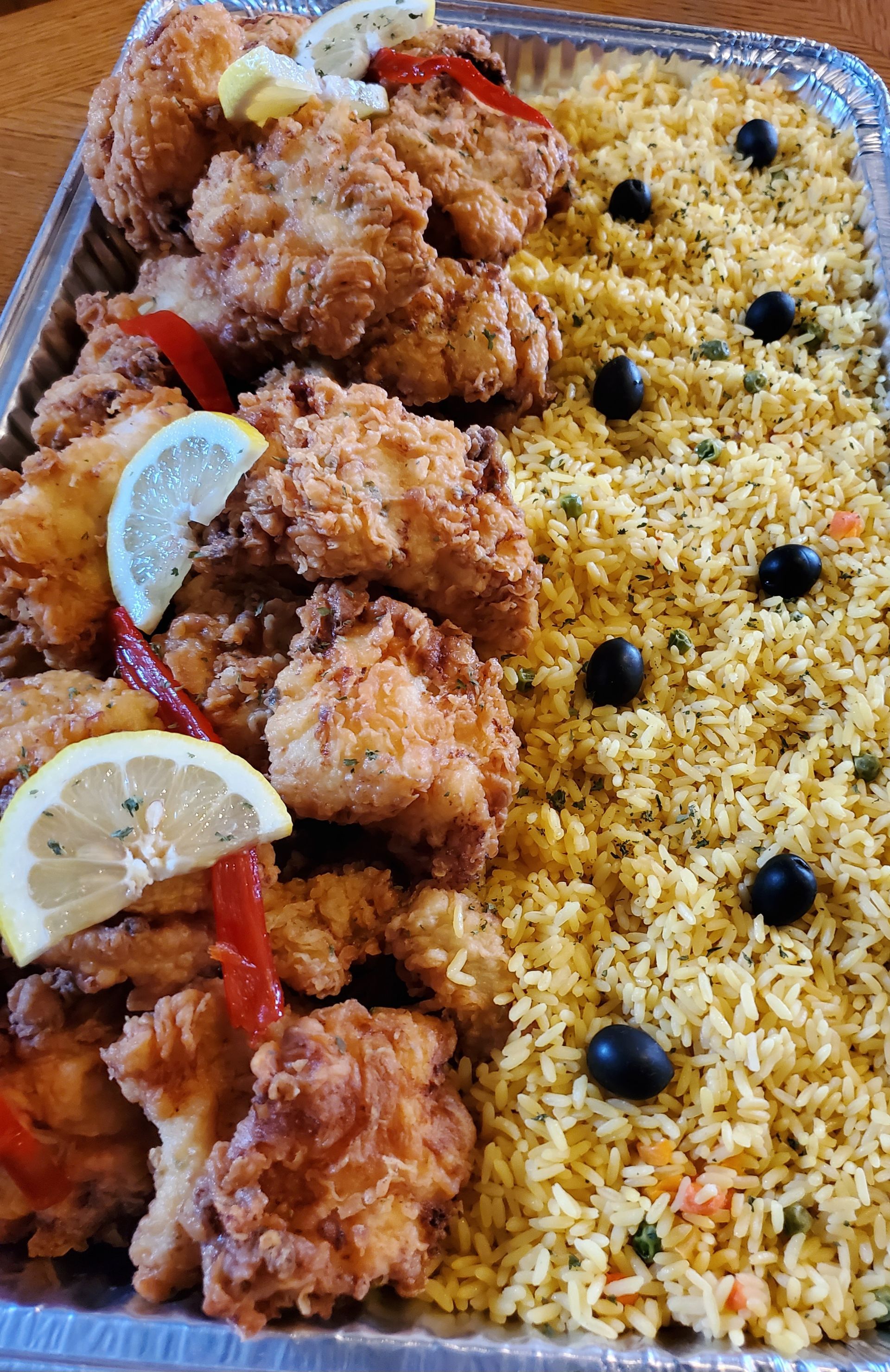 Fried chicken and yellow rice in a tray, garnished with lemons, red peppers, and black olives.