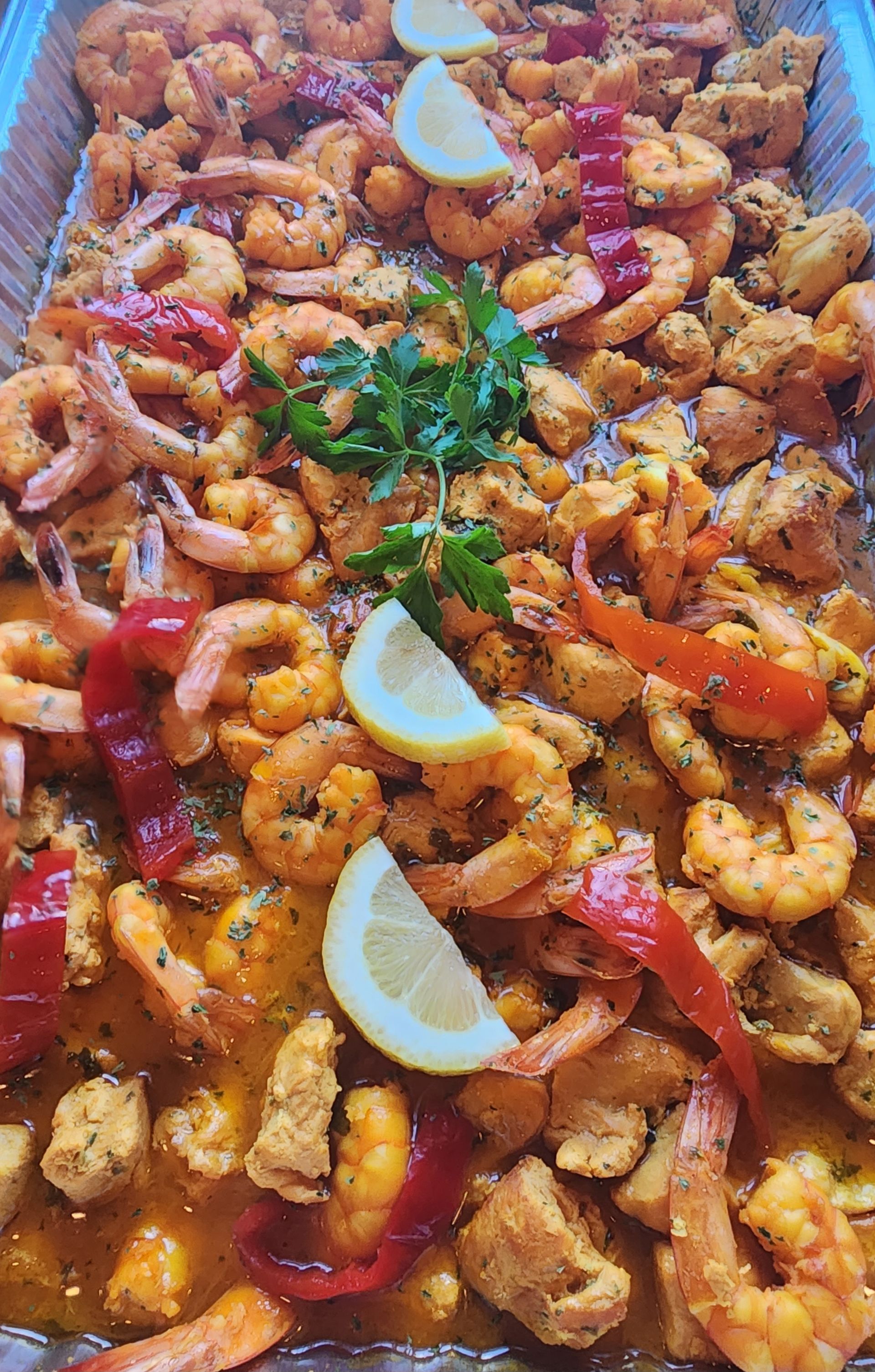 Tray of cooked shrimp, chicken, red peppers, lemon slices, and parsley.