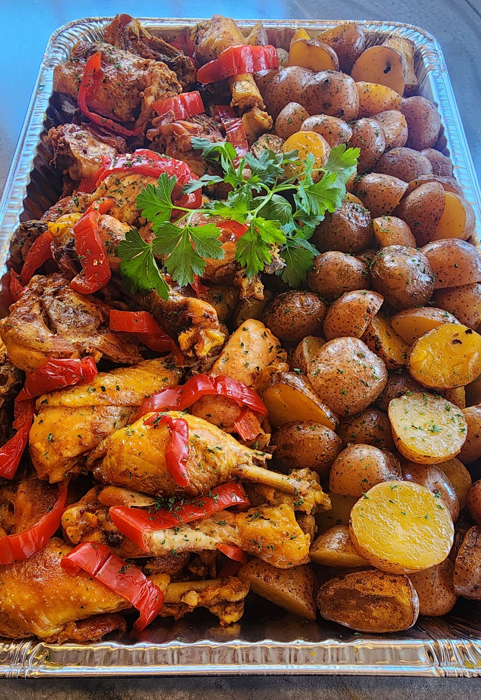 Tray of roasted chicken pieces with red peppers and seasoned potatoes.