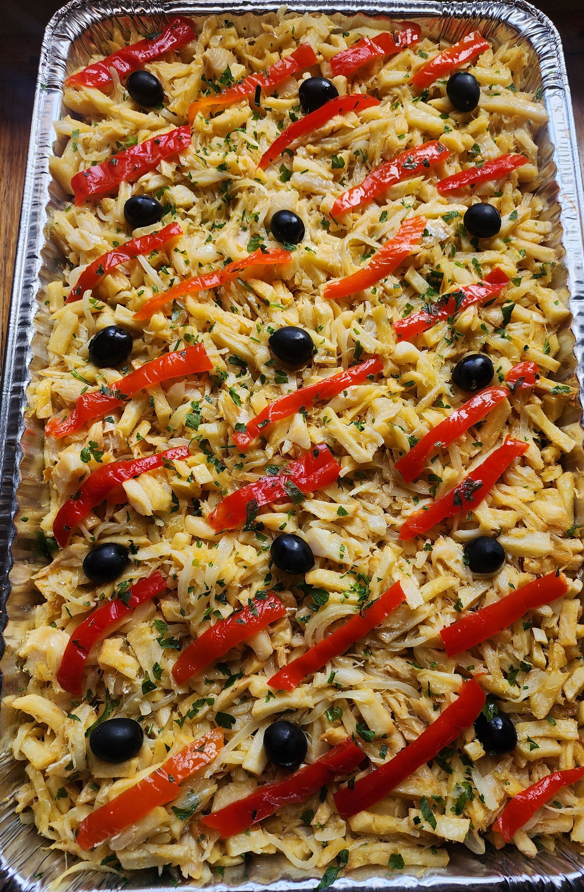 Baked dish in a foil pan: shredded potatoes and cod, red pepper strips, black olives.