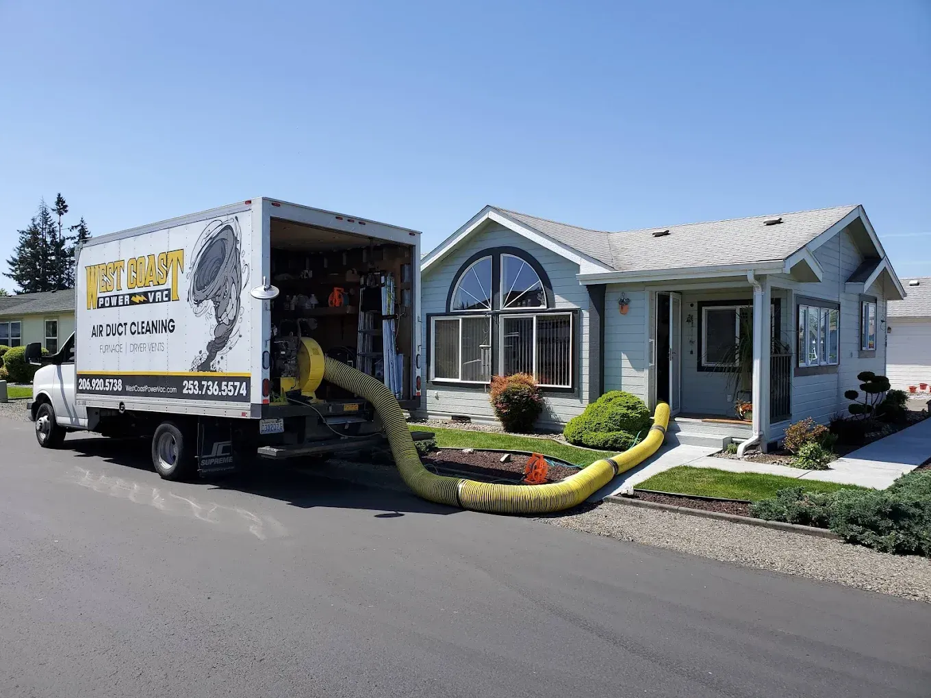 A truck with a large hose connected to a house for insulation. Sunlight, blue sky.