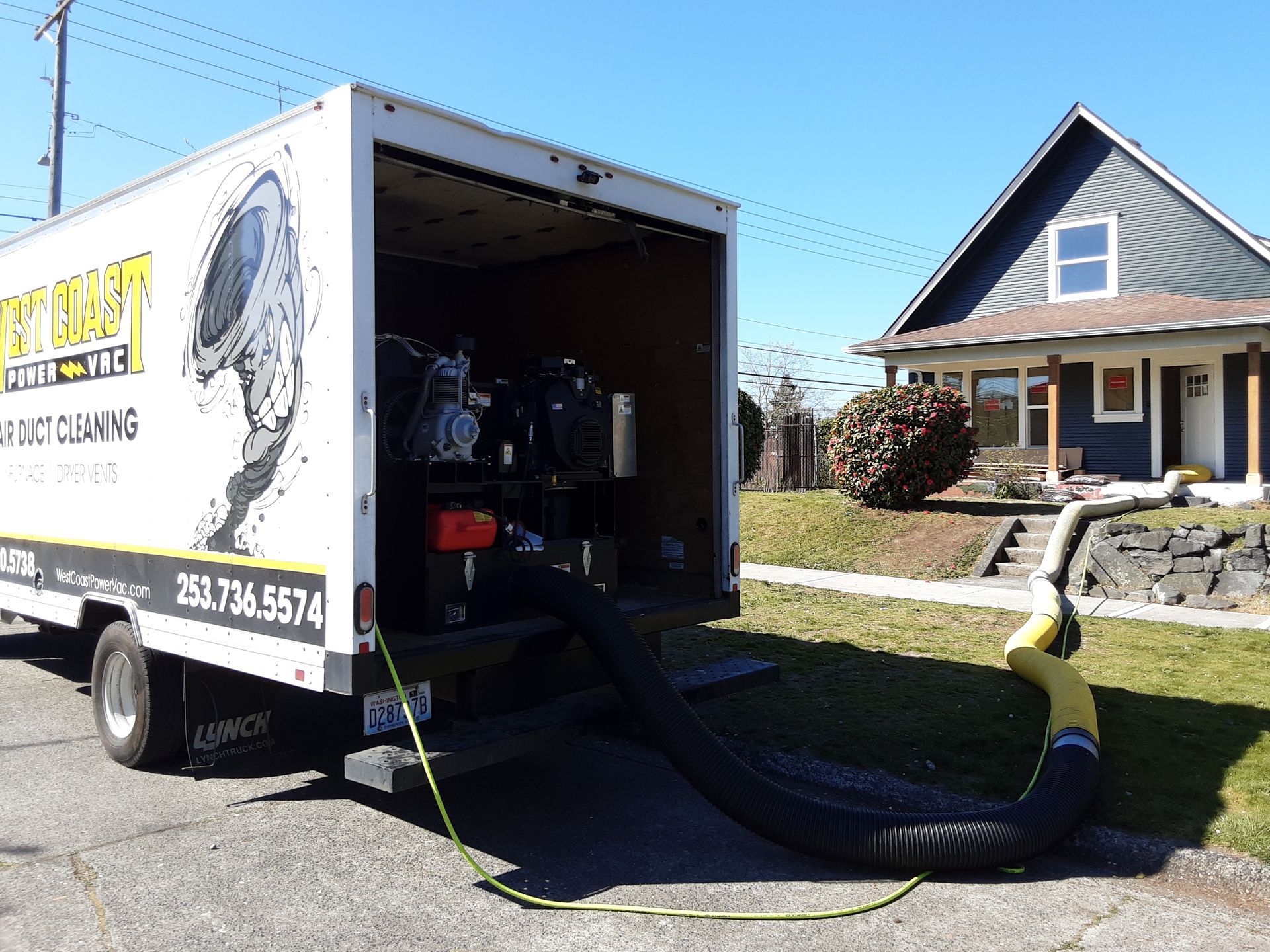 White service truck with open door, hose extended towards a house for dirt cleaning.