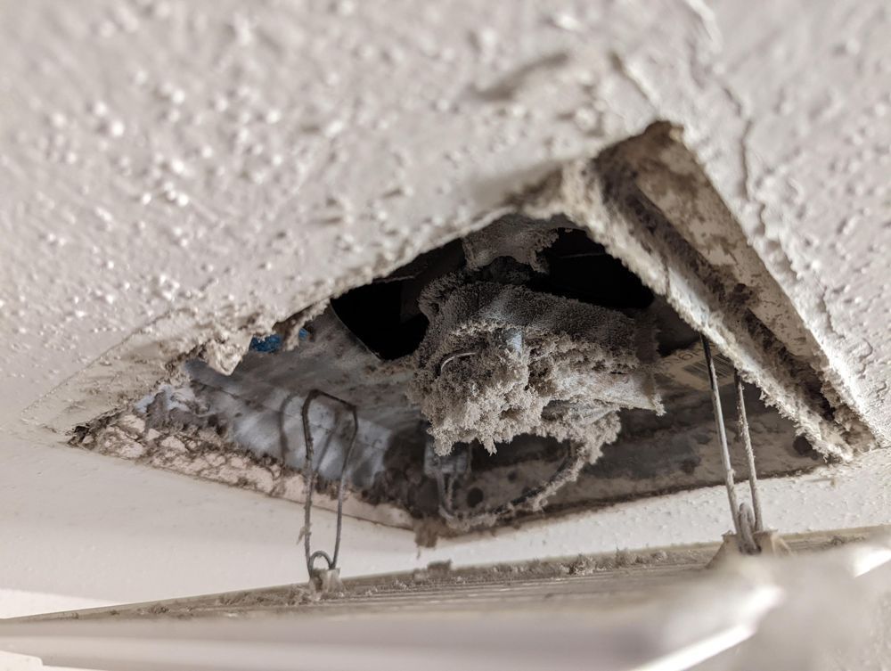 Dirty air vent clogged with dust and debris in a white ceiling.