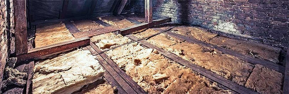 Interior of an unfinished attic with exposed insulation and wooden beams.