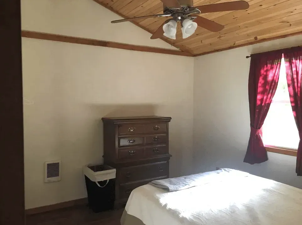 A modern bedroom with a cream mattress, grey upholstered headboard, a white vanity, and light grey walls.