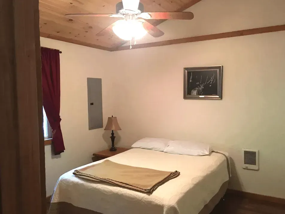 Modern bedroom with a white desk, grey upholstered headboard, beige mattress, and grey curtains against a light wall.
