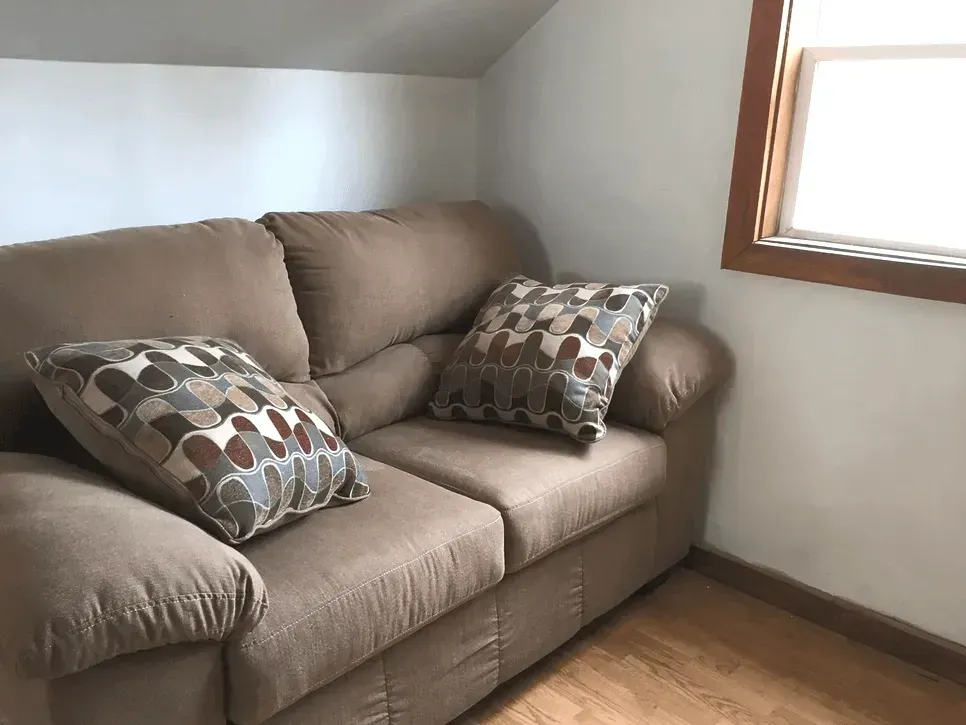A living room with a beige sofa, two patterned armchairs, an oval wooden coffee table, and a red and white rug.