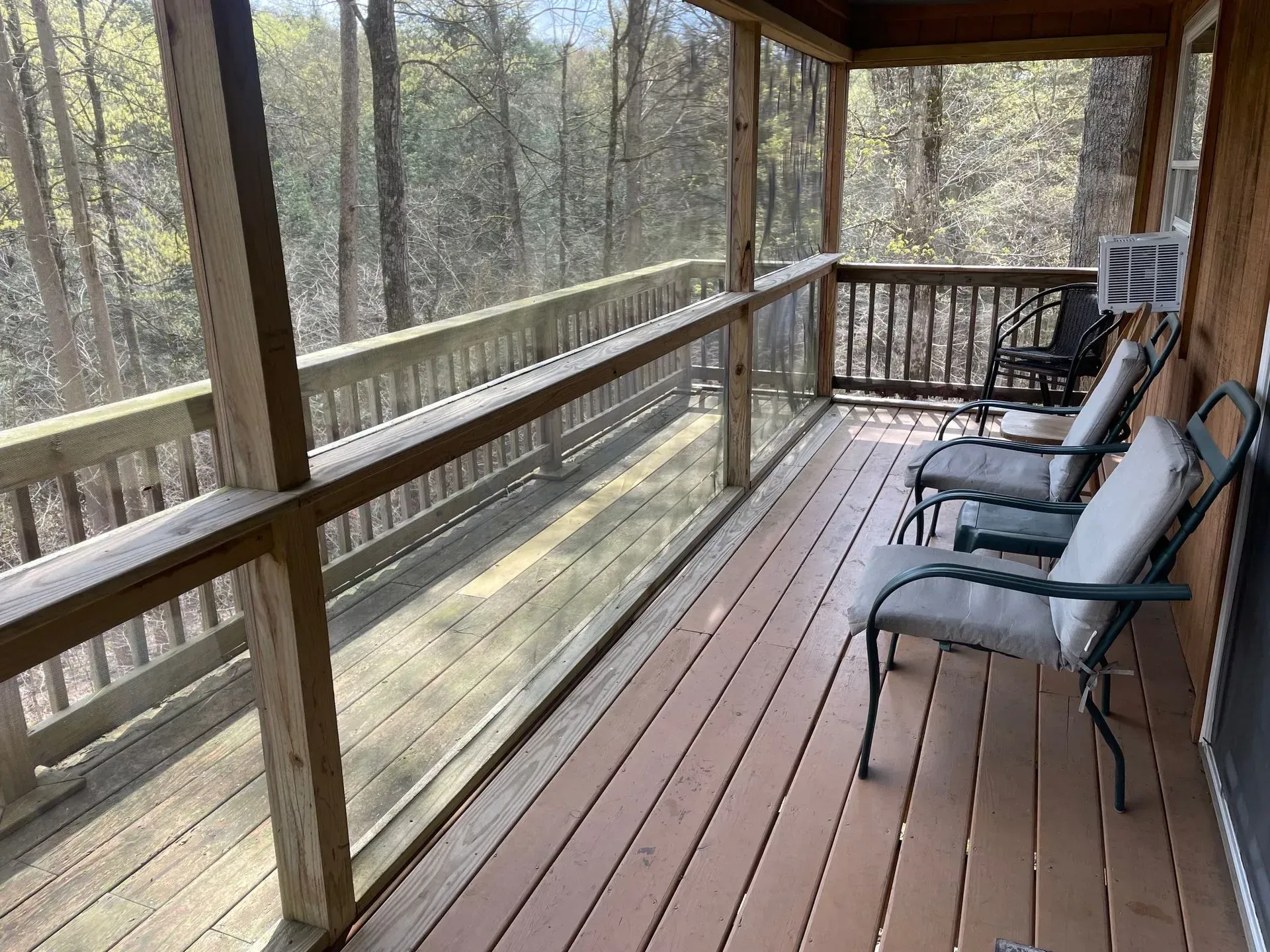 A screened-in porch with a blue sofa, wicker coffee table, dining set, and wooden ceiling with a ceiling fan.