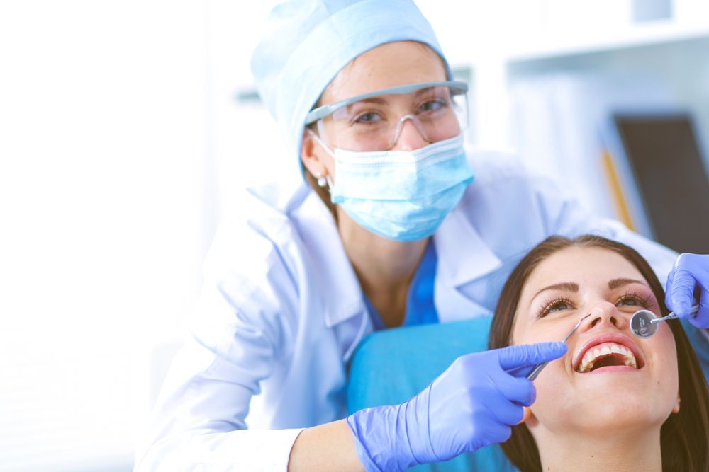 A woman is sitting in a dental chair while a dentist examines her teeth.