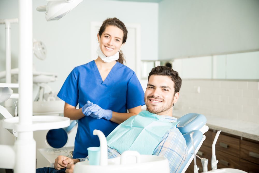 A man is sitting in a dental chair with a nurse standing next to him.