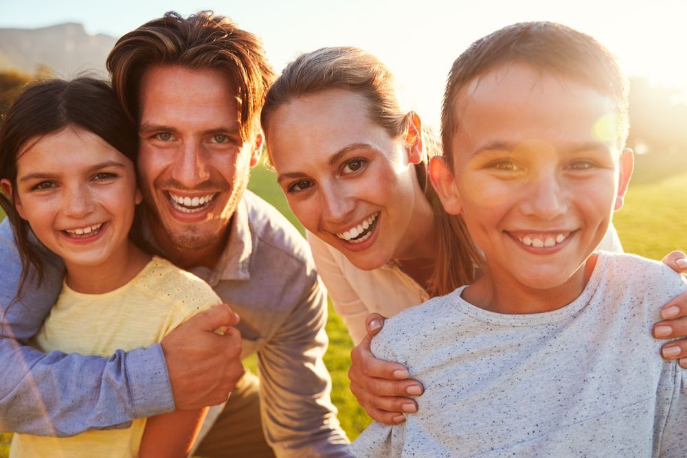 Family of four smiling, outdoors in sunlight.
