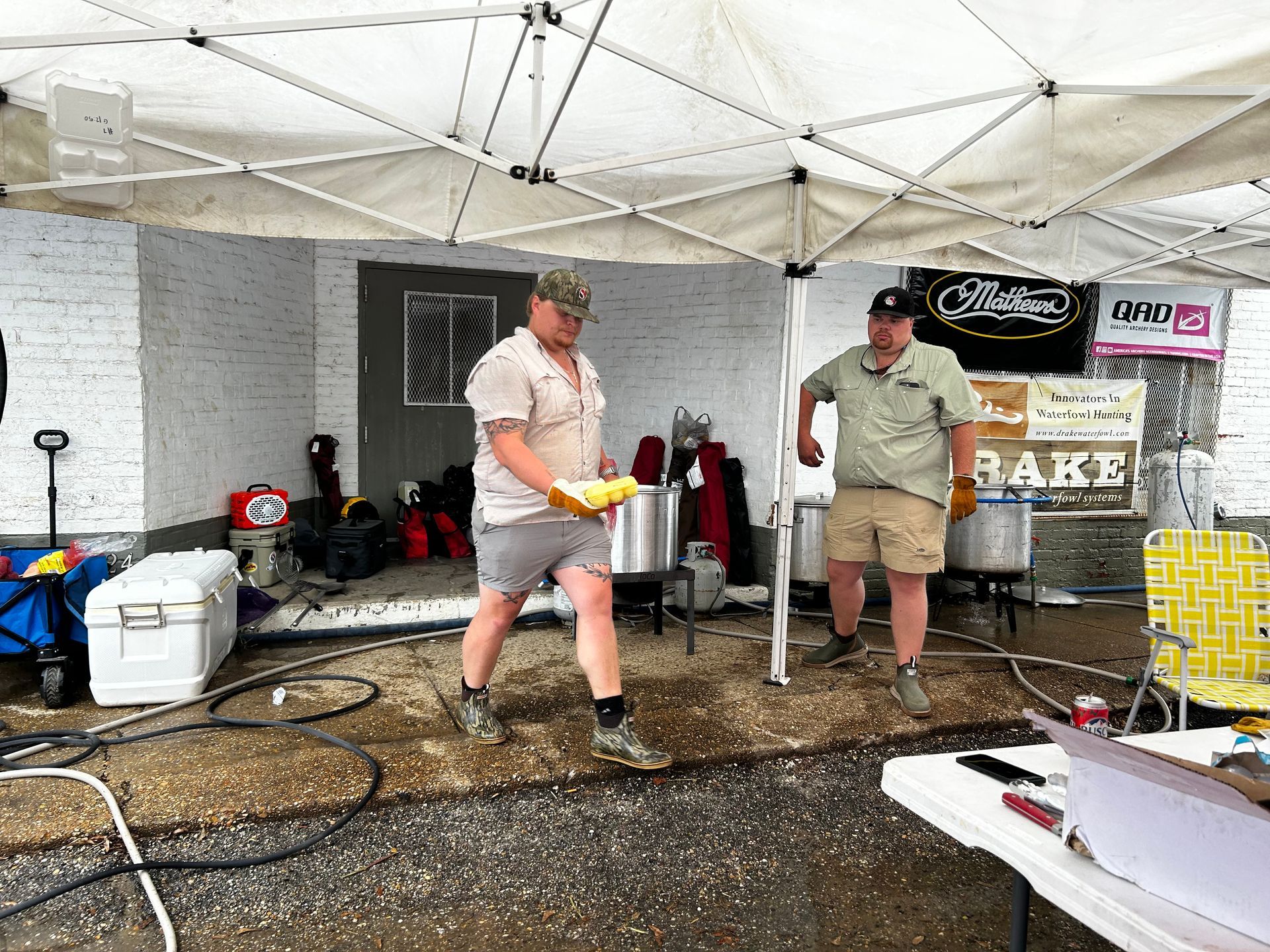 Two men are standing under a tent in front of a building.