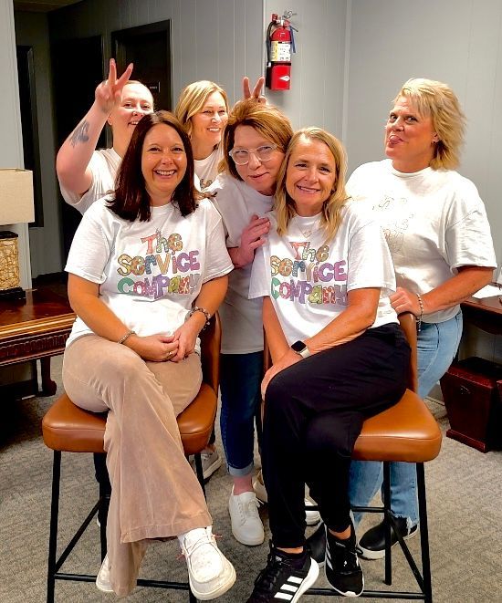 A group of women are posing for a picture while wearing shirts that say the service company