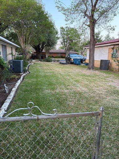 Chain-link gate opening to a grassy backyard with trees, a blue pickup truck, and a small shed.